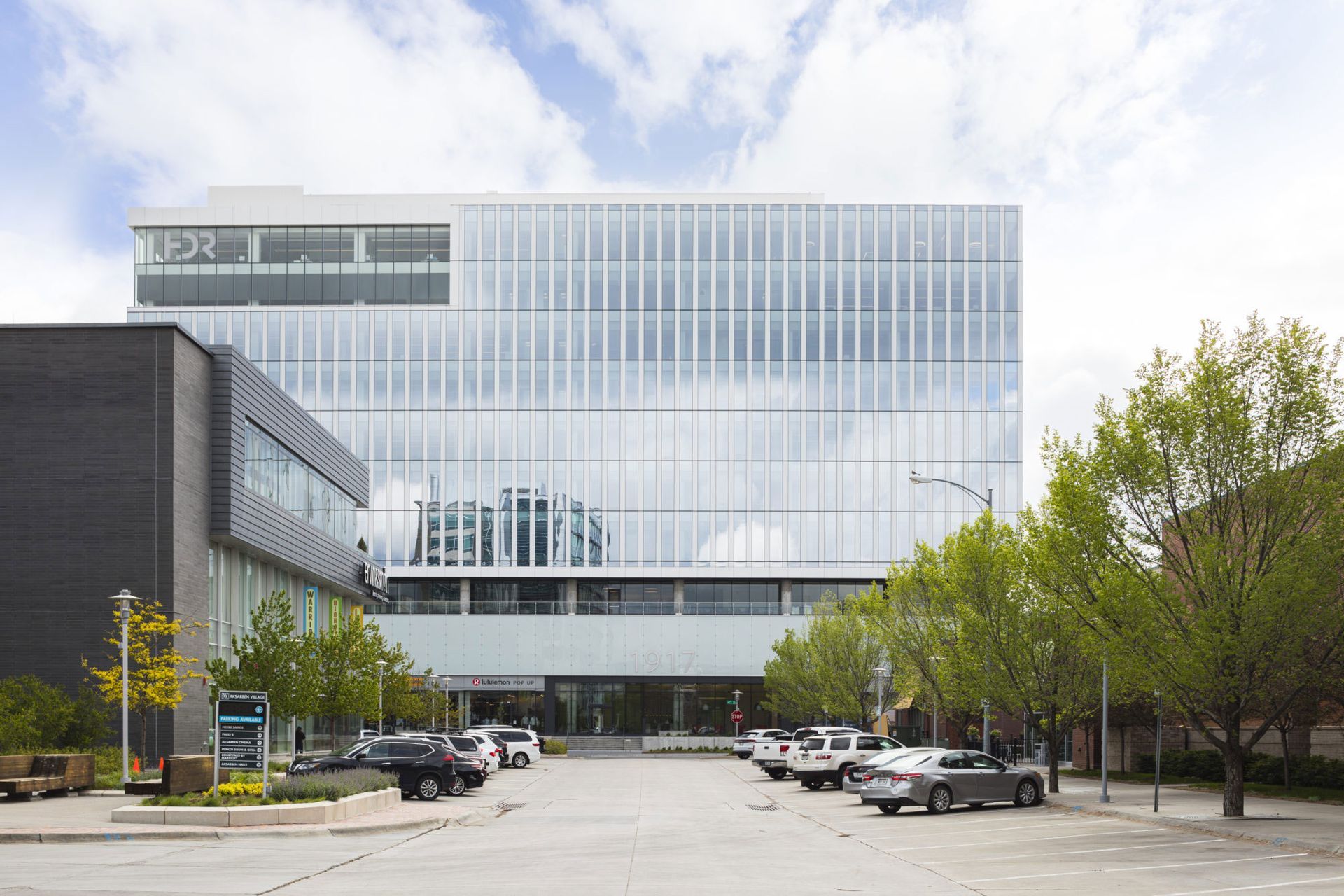 Modern glass office building with a tree-lined street and parked cars in front