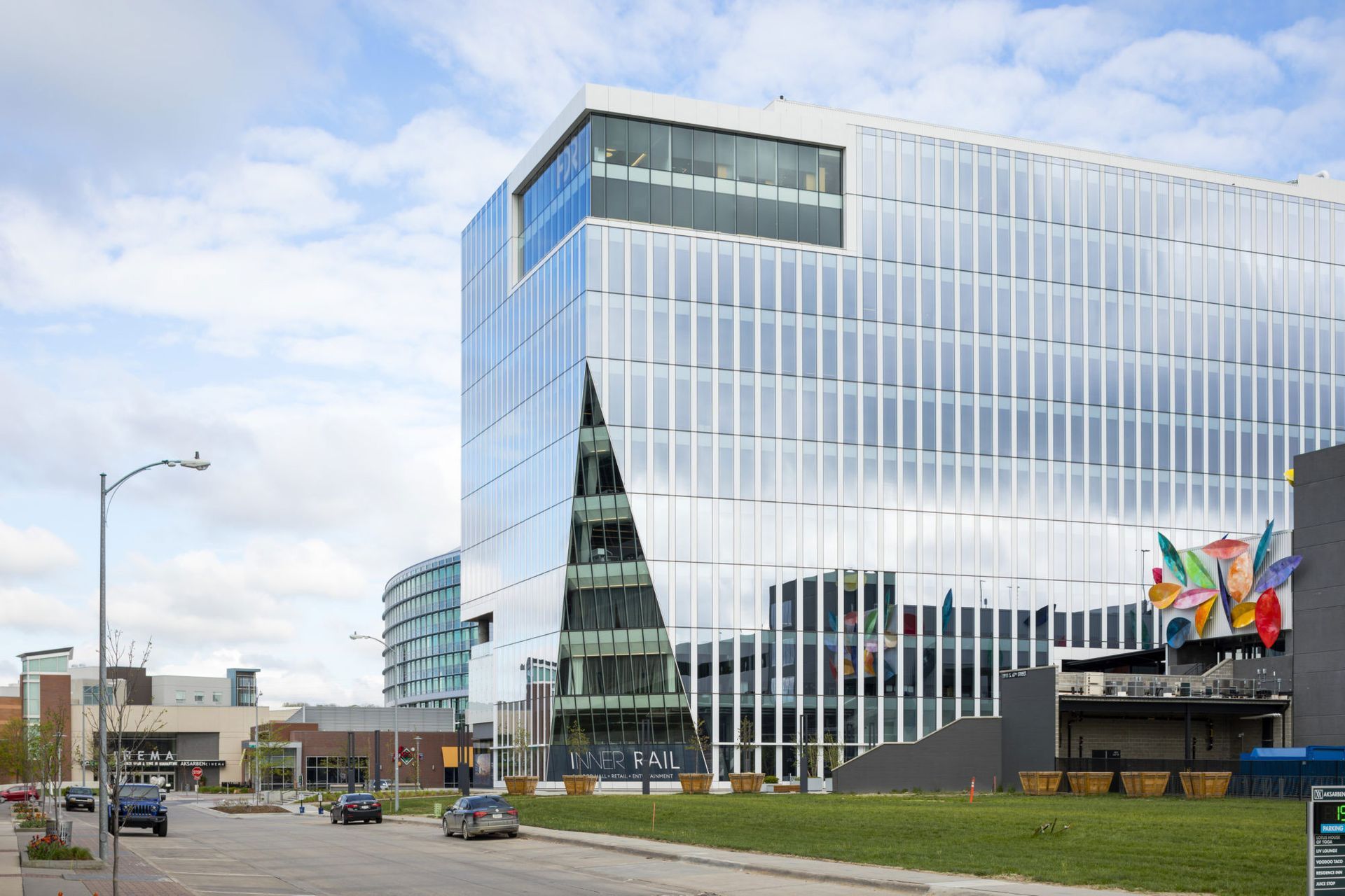 Modern glass office building with flags, viewed from a street under a cloudy sky