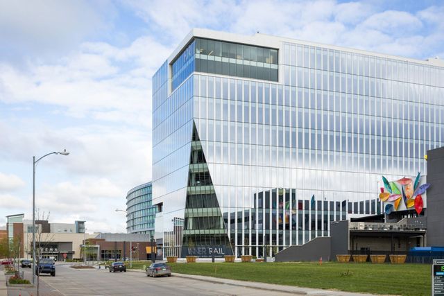 Modern glass office building with a triangular entrance and colorful flags by the road