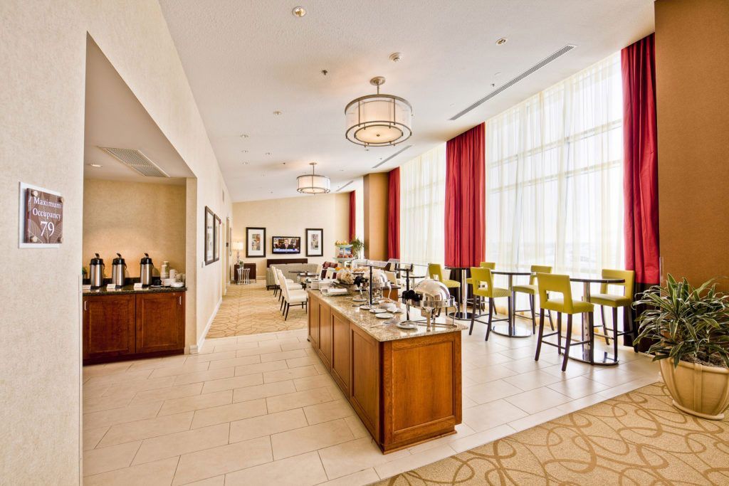 Bright dining room with long buffet tables, yellow chairs, red curtains, and large windows