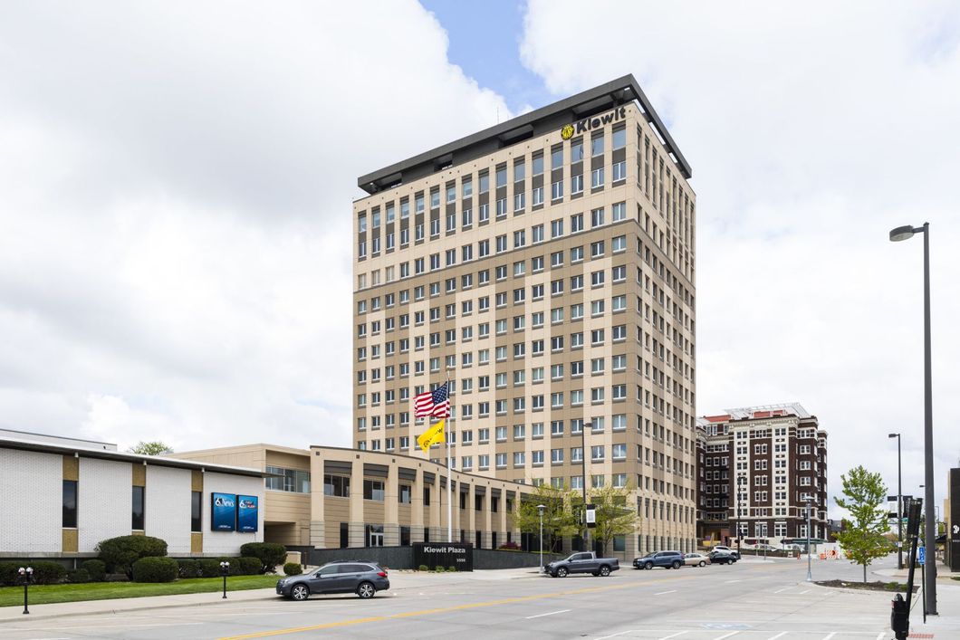 Tall beige office building beside a low white building on a city street under a cloudy sky