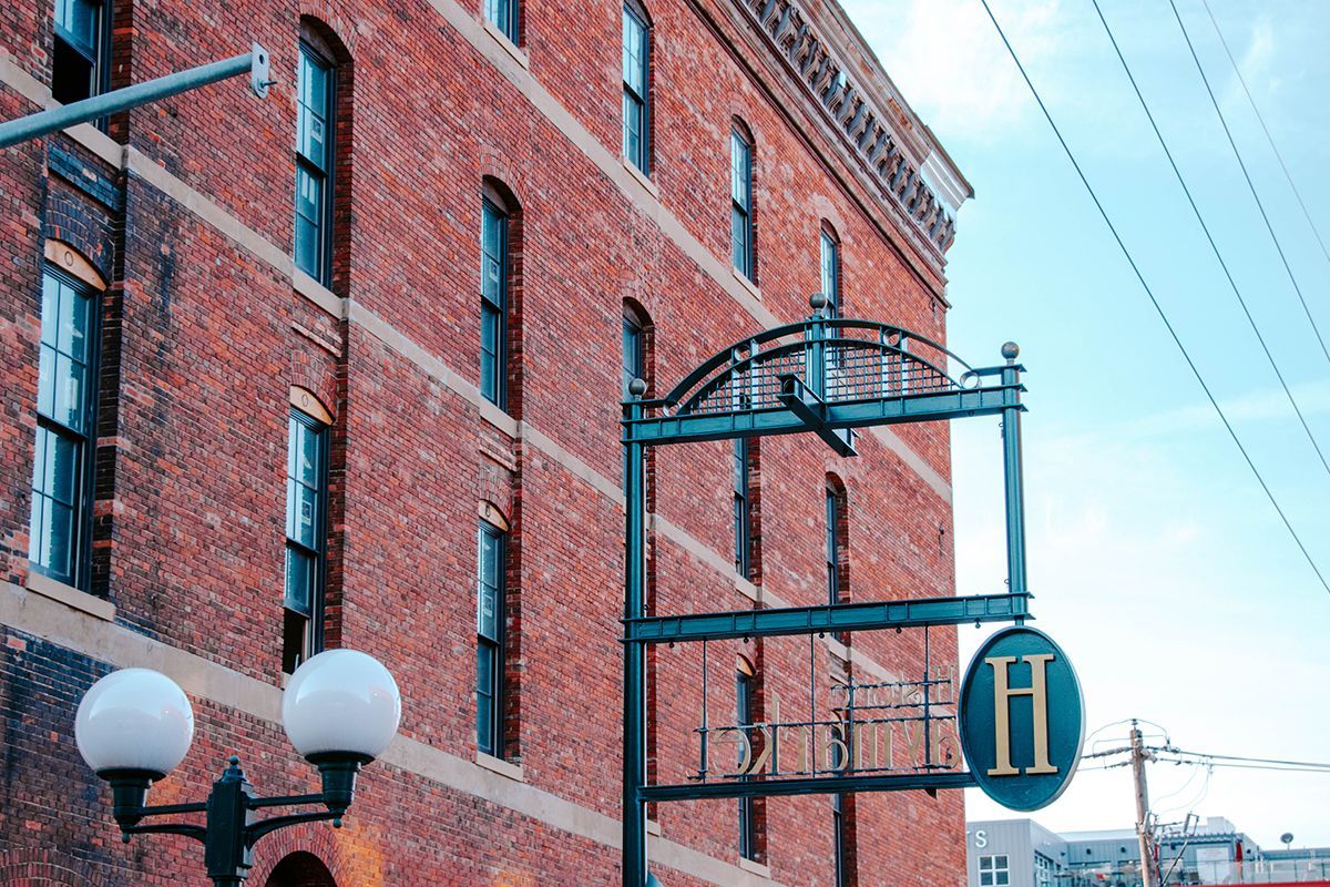 Brick building with black metal sign bracket and blue circular “H” sign on a city street