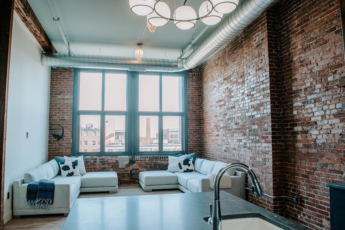 Bright loft living room with exposed brick walls, large windows, and white sectional sofas