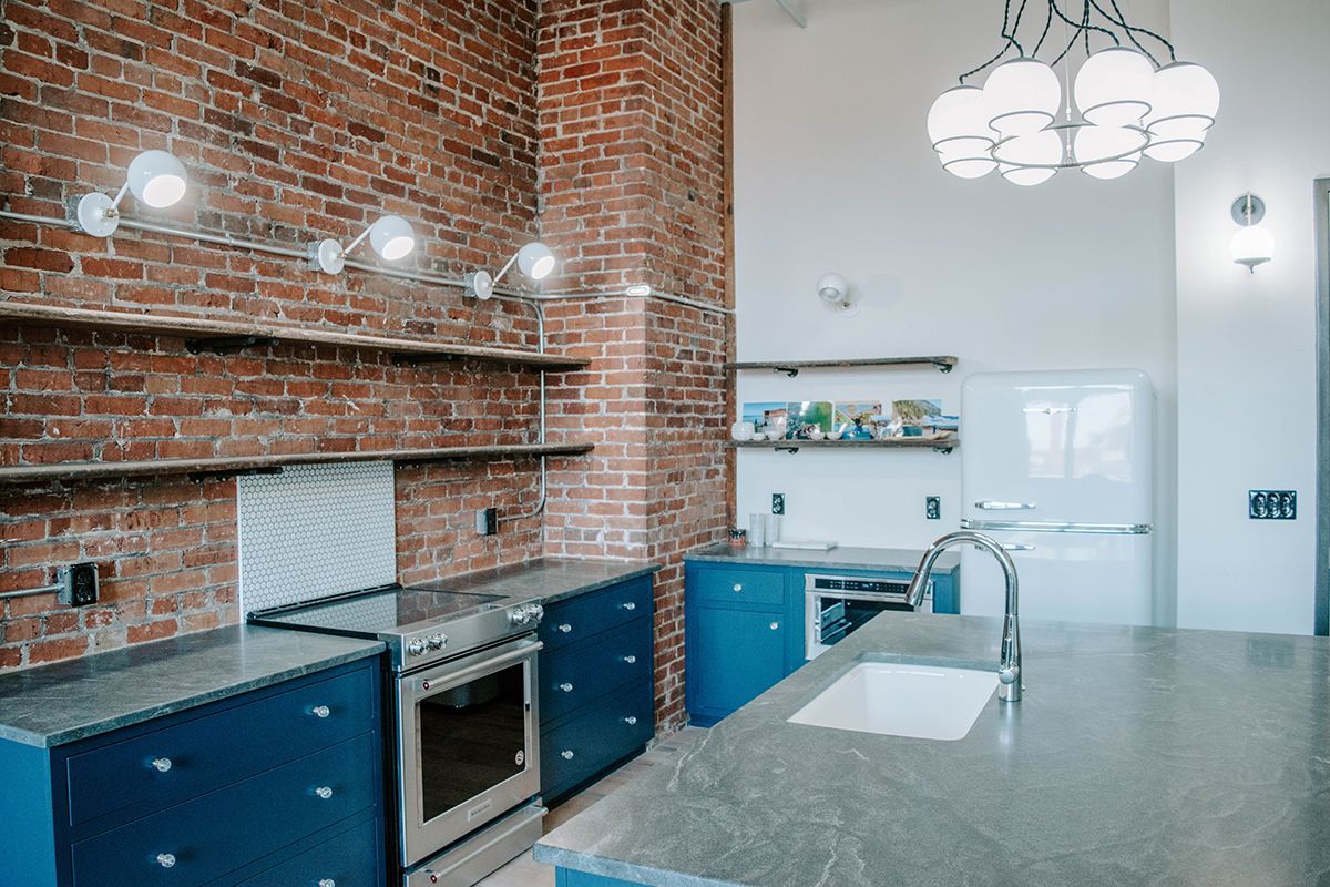 Modern kitchen with exposed brick wall, blue cabinets, and large island countertop
