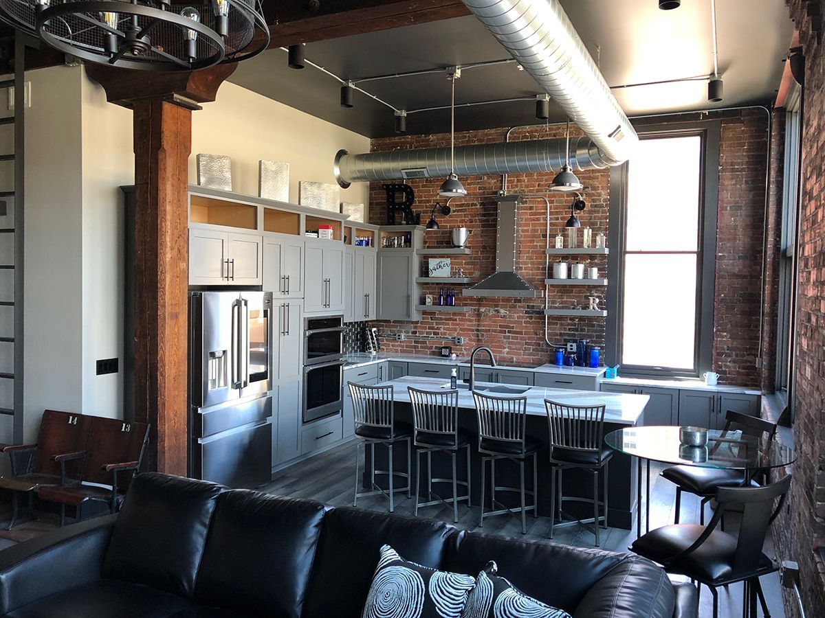 Modern loft kitchen with brick wall, island seating, stainless appliances, and exposed beams