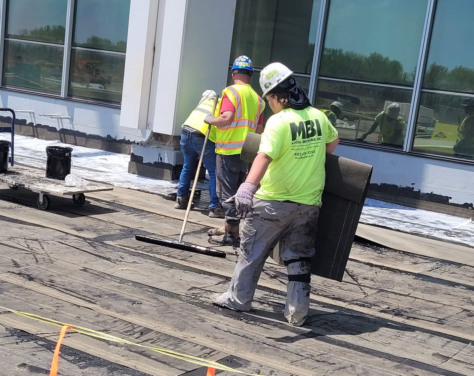 Two workers in neon safety vests installing roofing material on a flat roof