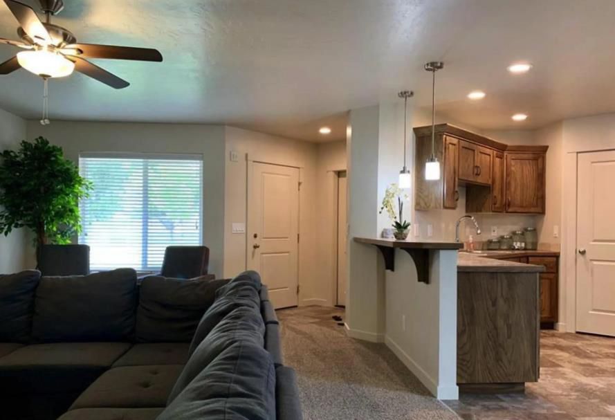 A living room with a couch, ceiling fan, and kitchen.