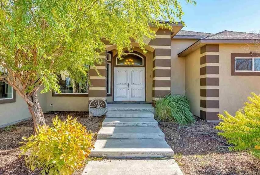 A house with stairs leading up to the front door and a tree in front of it.