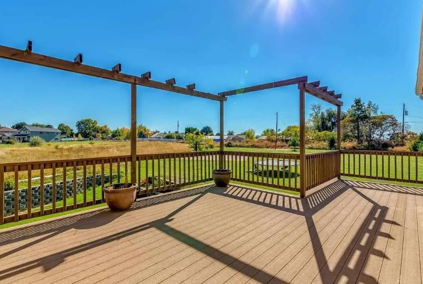 A large wooden deck with a pergola and a view of a field.