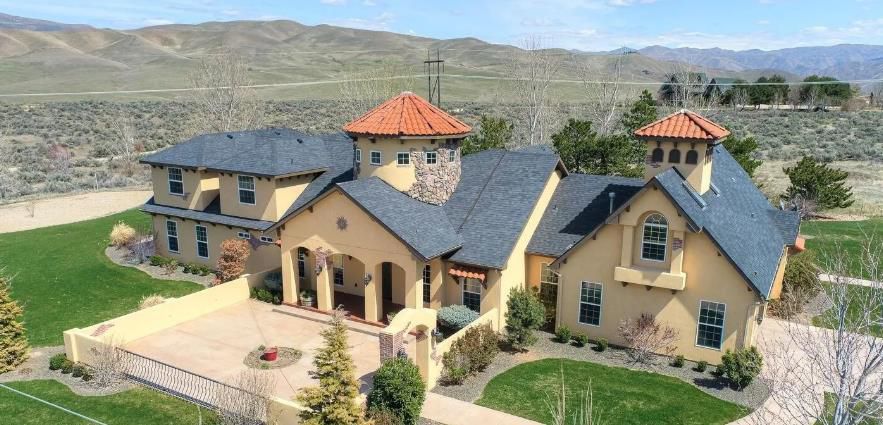 An aerial view of a large house in the middle of a field with mountains in the background.