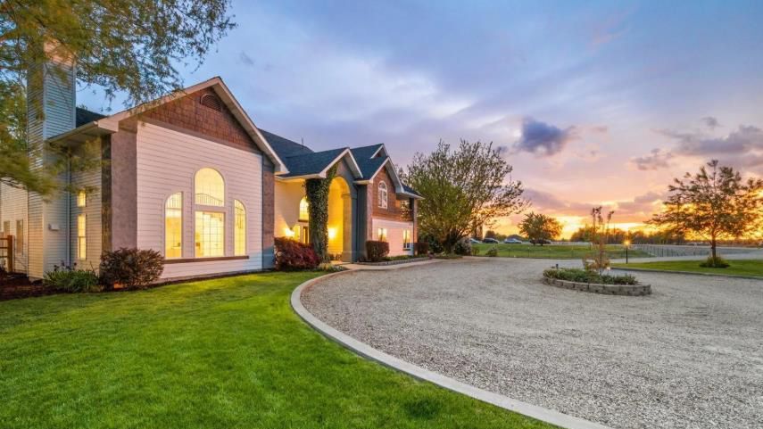 A large white house with a gravel driveway in front of it at sunset.
