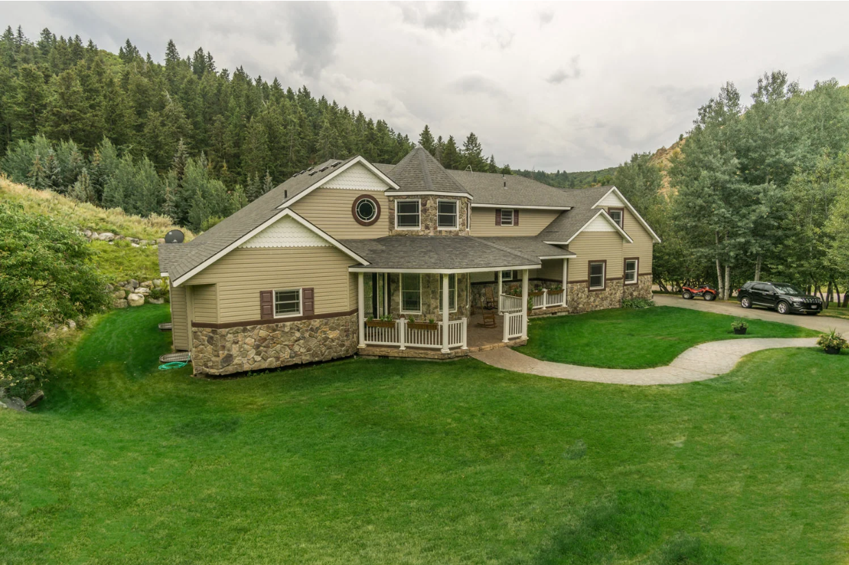 A large house is sitting on top of a lush green hillside surrounded by trees