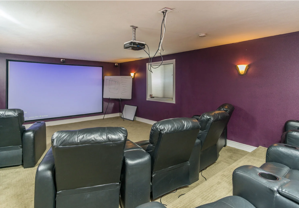A home theater with purple walls and black leather chairs and a projector screen
