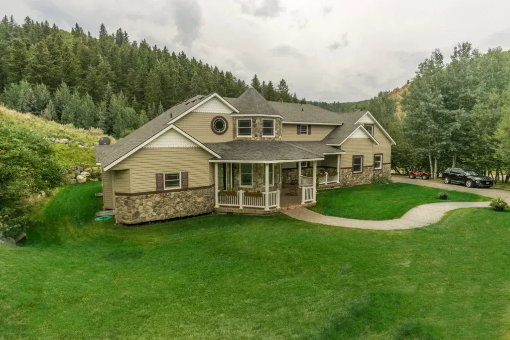 A large house is sitting on top of a lush green hillside surrounded by trees.