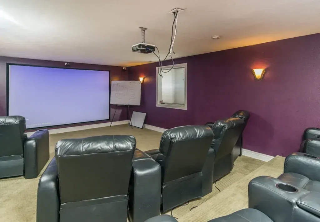 A home theater with purple walls and black leather chairs and a projector screen.