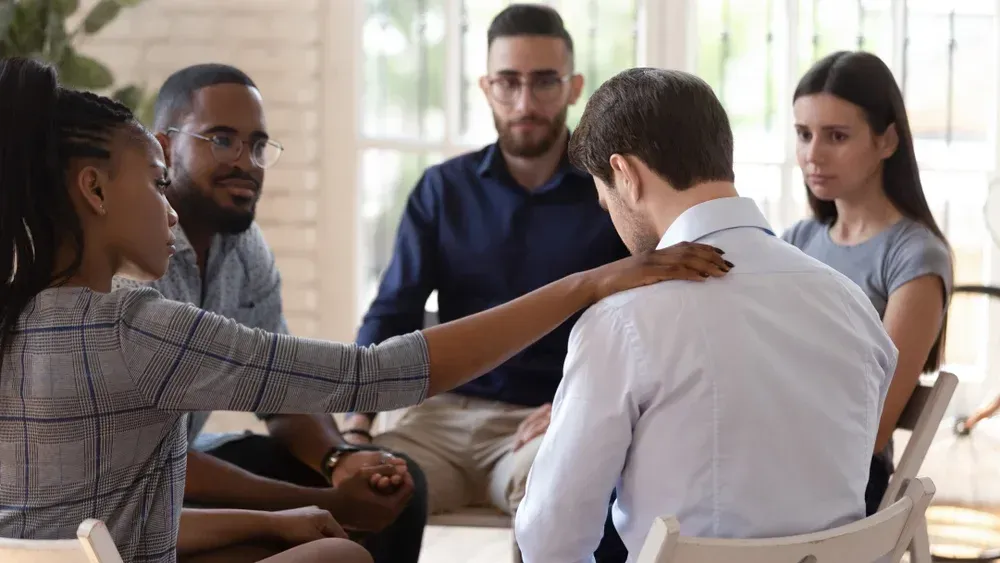 A group of people are sitting around a table with their arms around each other.