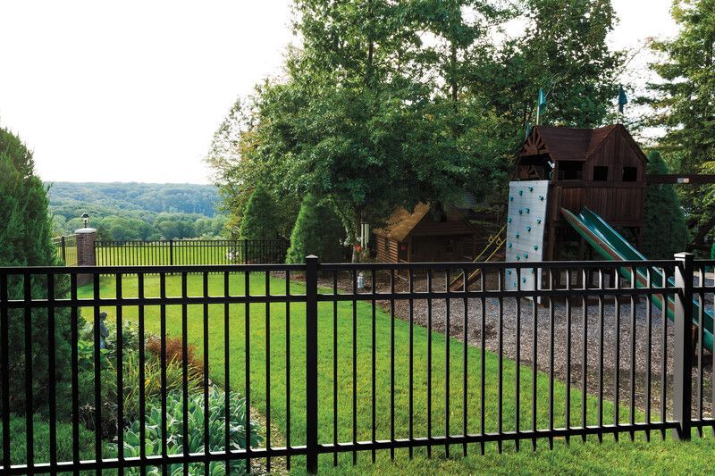Backyard with black fence, green lawn, large tree, and a small play structure beside a house
