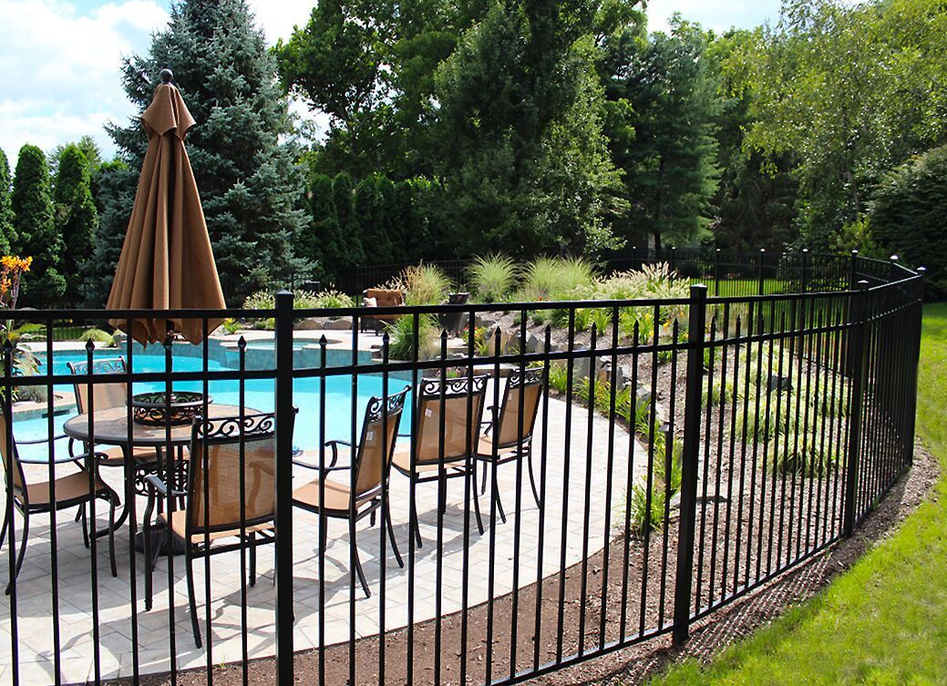 Backyard pool with lounge chairs, umbrella, and black metal fence surrounded by trees