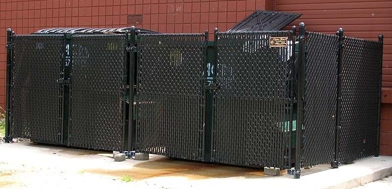 Black metal storage cages lined up outdoors against a brick wall.