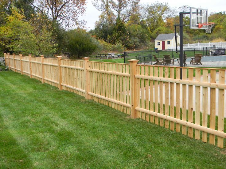 Wooden fence lining a green lawn beside a basketball court on an overcast day
