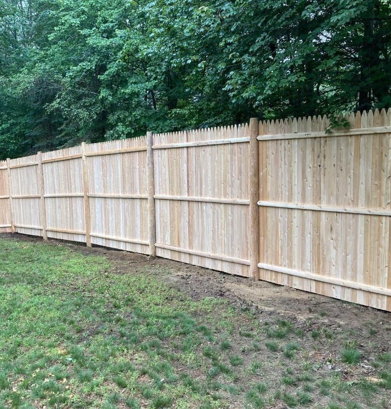 Wooden fence along a grassy yard with dense green trees behind it