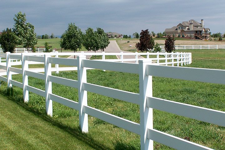 White fence curving through a green field toward a large house under a cloudy sky