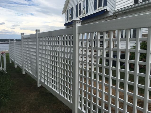 White lattice fence along a coastal house with blue shutters and a driveway at sunset