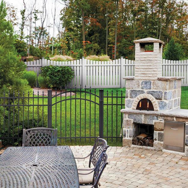 Patio with metal table and chairs, stone outdoor fireplace, black fence, and white privacy fence