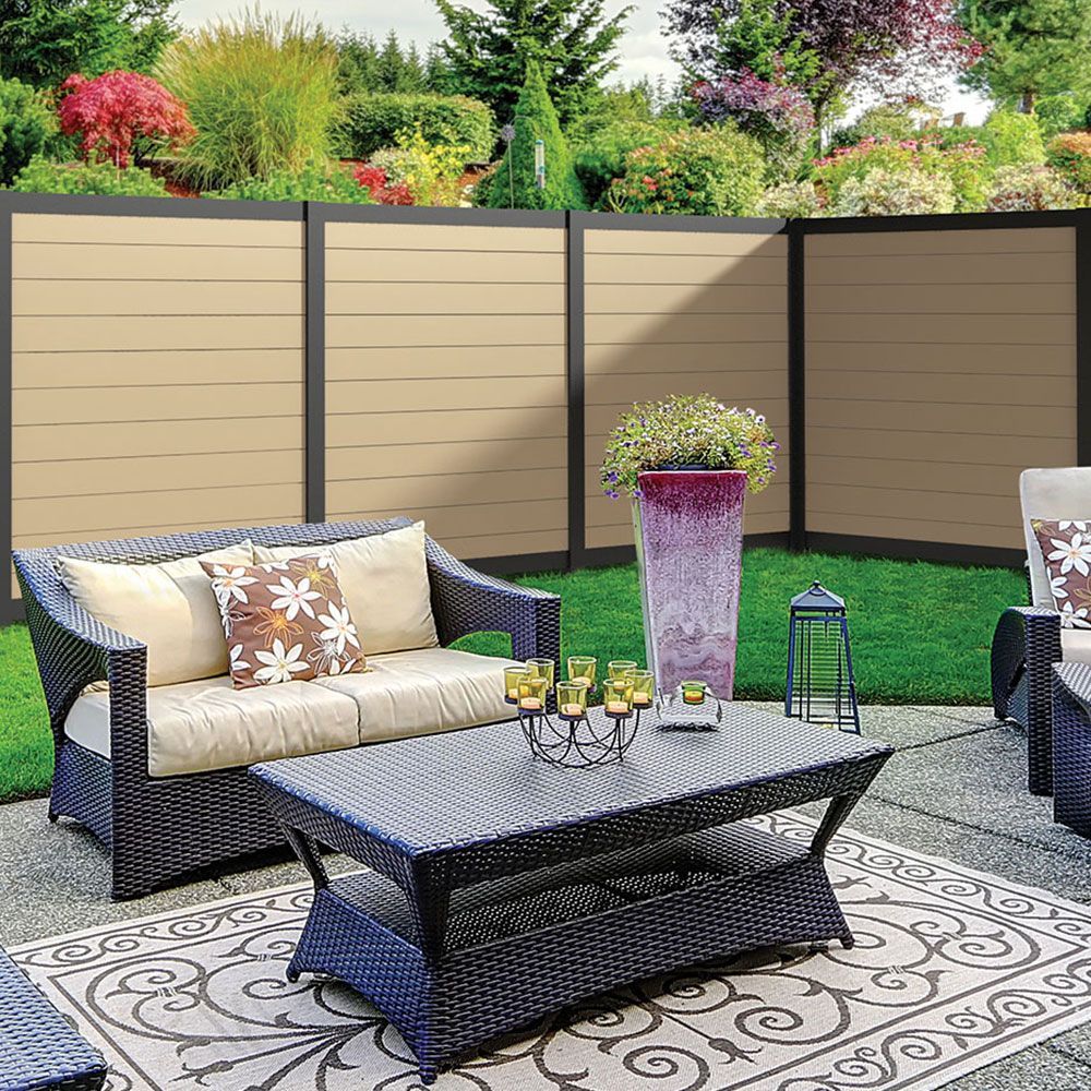Patio seating area with wicker sofa, coffee table, flower vase, lantern, and decorative fence backdrop