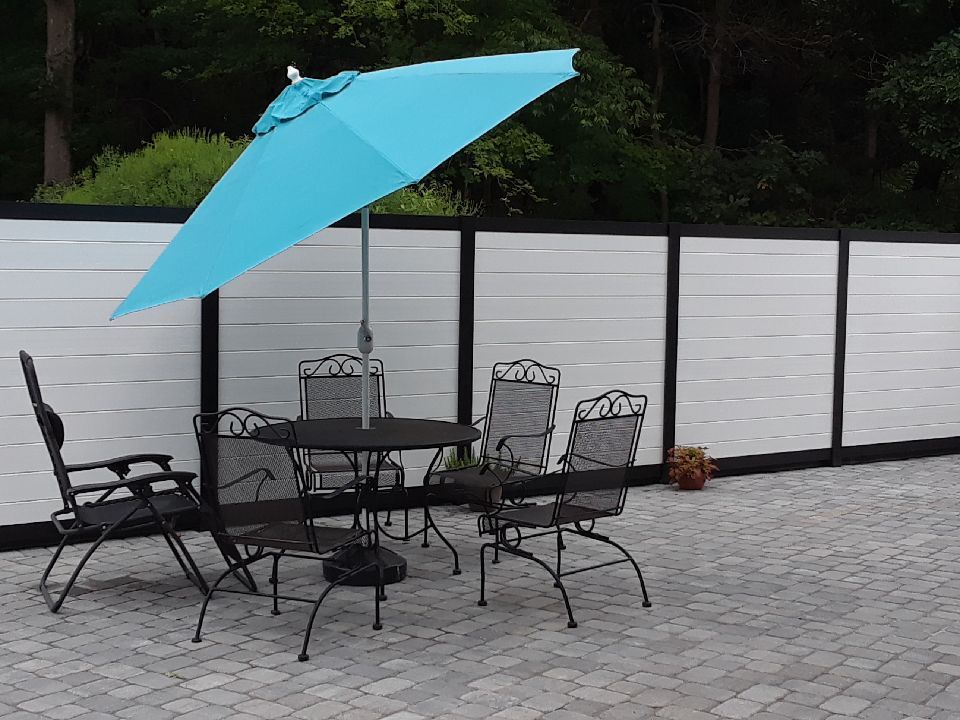 Patio table and chairs under a turquoise umbrella beside a white fence