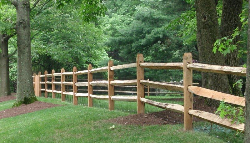Wooden split-rail fence along a grassy wooded path with lush green trees.
