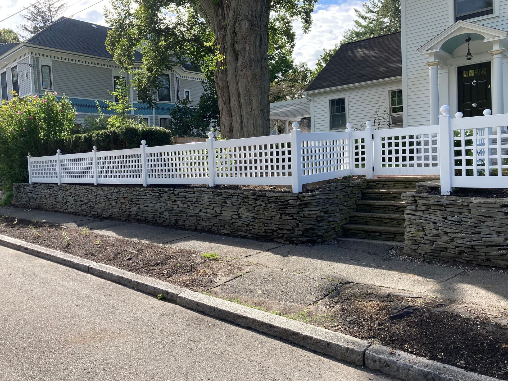 Stone retaining wall with white fence and house along a quiet street