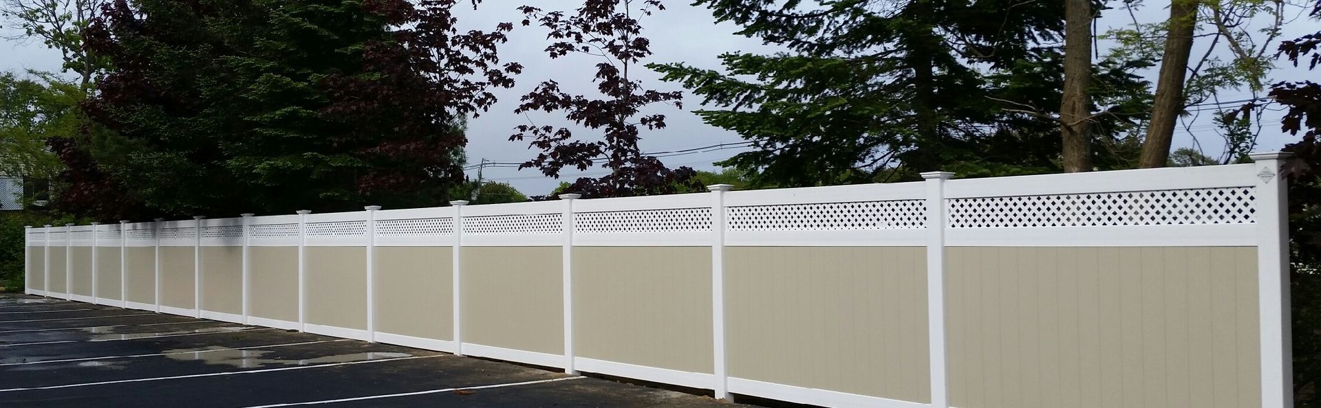 White vinyl privacy fence along a tree-lined roadside under a dark sky