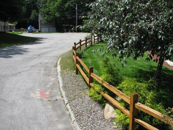Curving gravel road beside a wooden fence and green grass in a wooded area