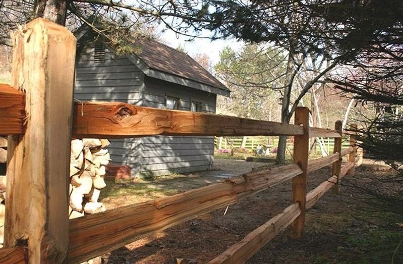 Wooden fence beside a rustic house in a wooded yard with bare trees and winter light