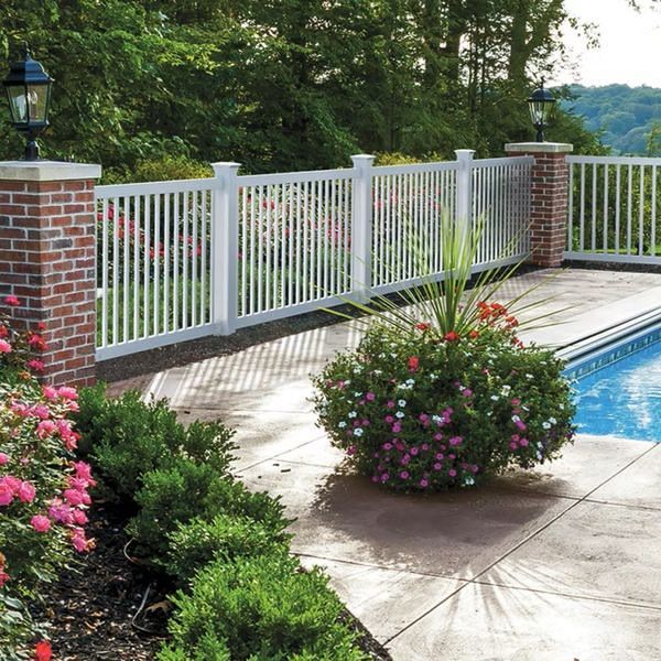 Backyard pool with white fence, brick posts, and flowering shrubs by a stone patio