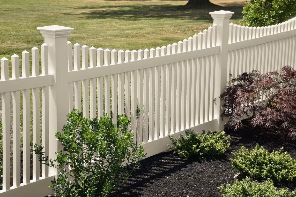 White picket fence along a landscaped yard with green shrubs and dark mulch