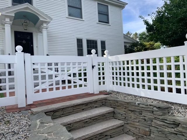 Front entry with white lattice fence and stone steps leading to a gray house