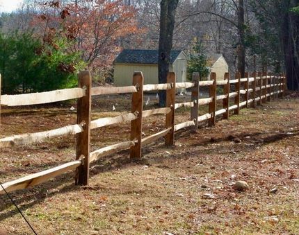 Wooden split-rail fence along a wooded rural yard with a small house in the background