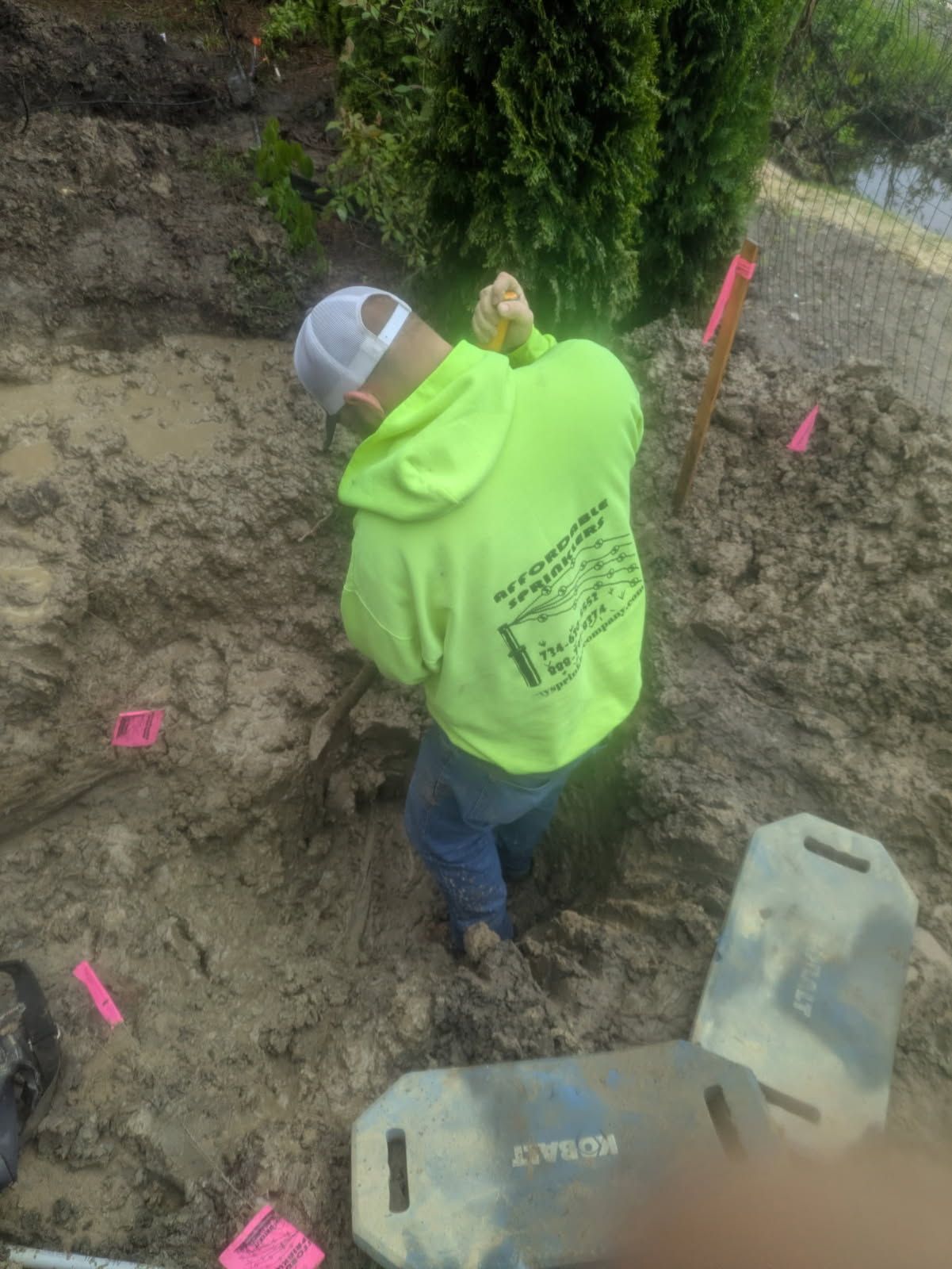 Person in neon green hoodie digs in dirt, surrounded by pink flags and Cobalt boards.