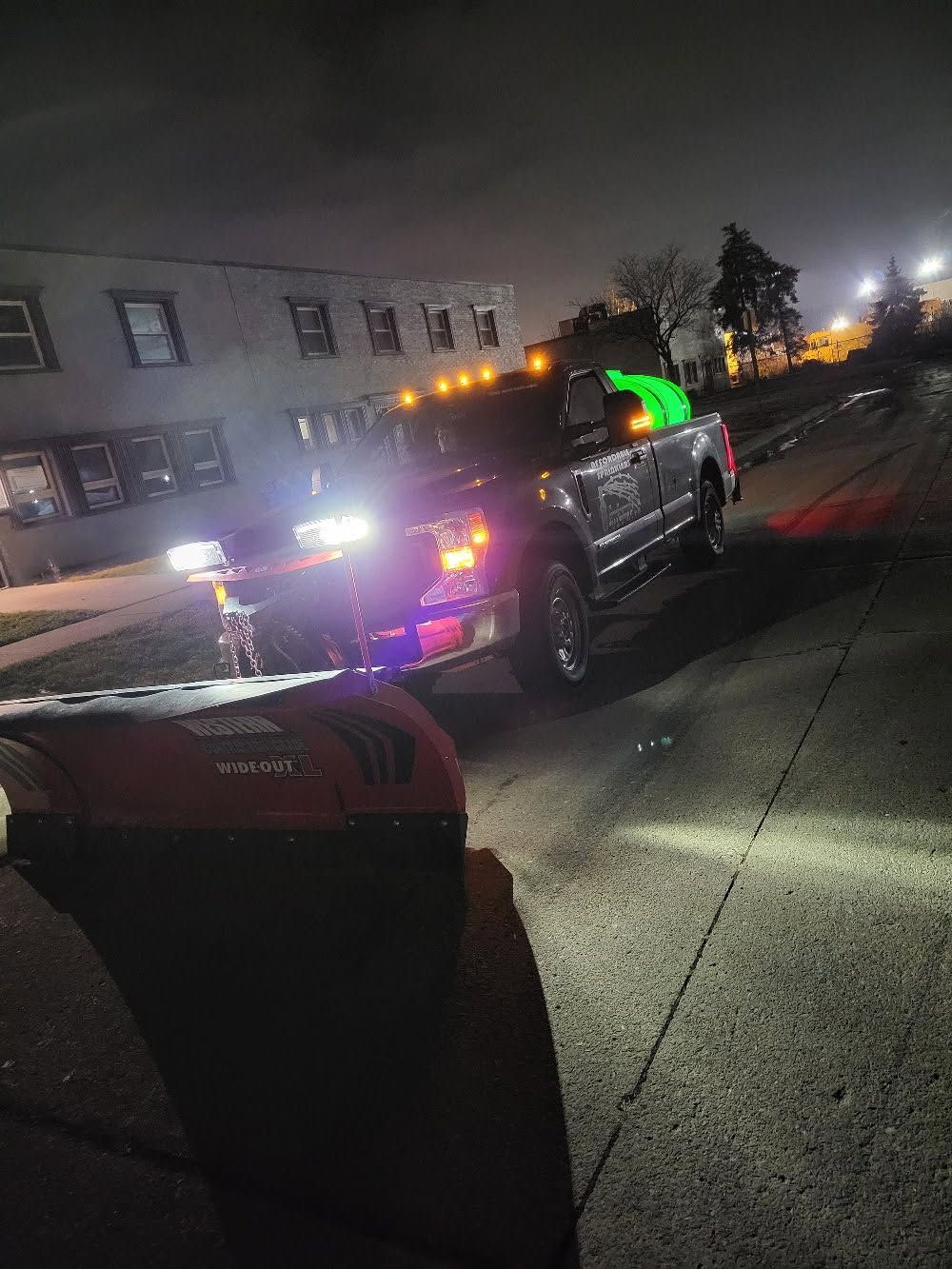 A black pickup truck parked on a dark street at night, headlights illuminated, with a bright orange object in the foreground.
