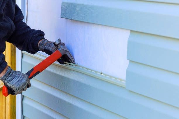 Gloved worker using a red pry bar to remove siding from a house exterior