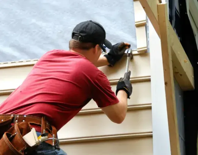 Worker installing siding on a house exterior, using a drill near a window