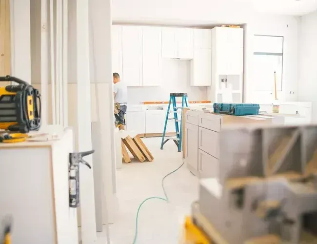 Bright kitchen under renovation with white cabinets, a ladder, and tools on the floor