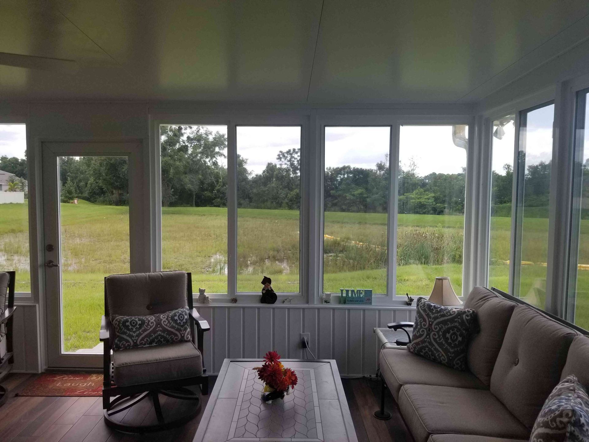 Sunroom with wicker chair, sofa, and coffee table overlooking a grassy field through large windows
