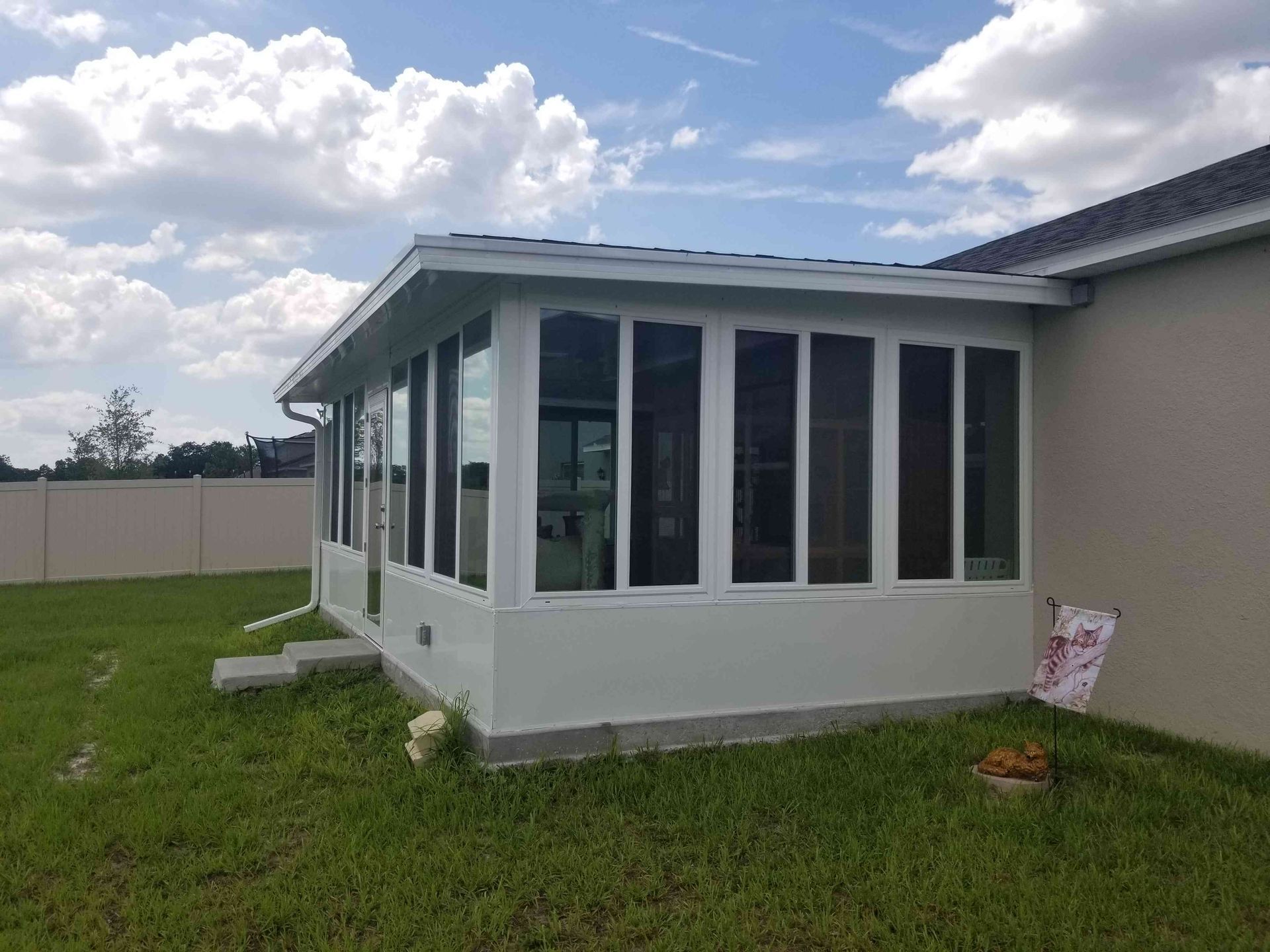 White sunroom addition with tall windows on a house, set beside a grassy yard under a cloudy sky