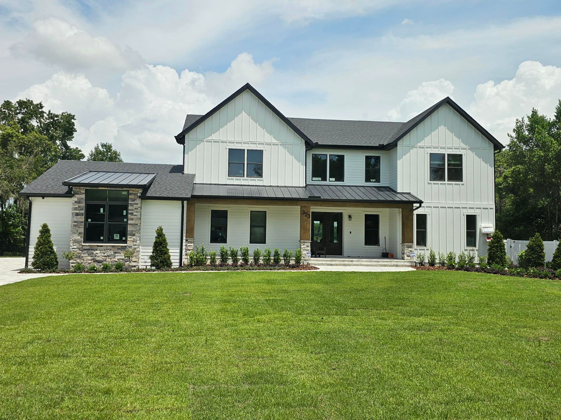Modern two-story white house with dark roof and large green lawn under a partly cloudy sky