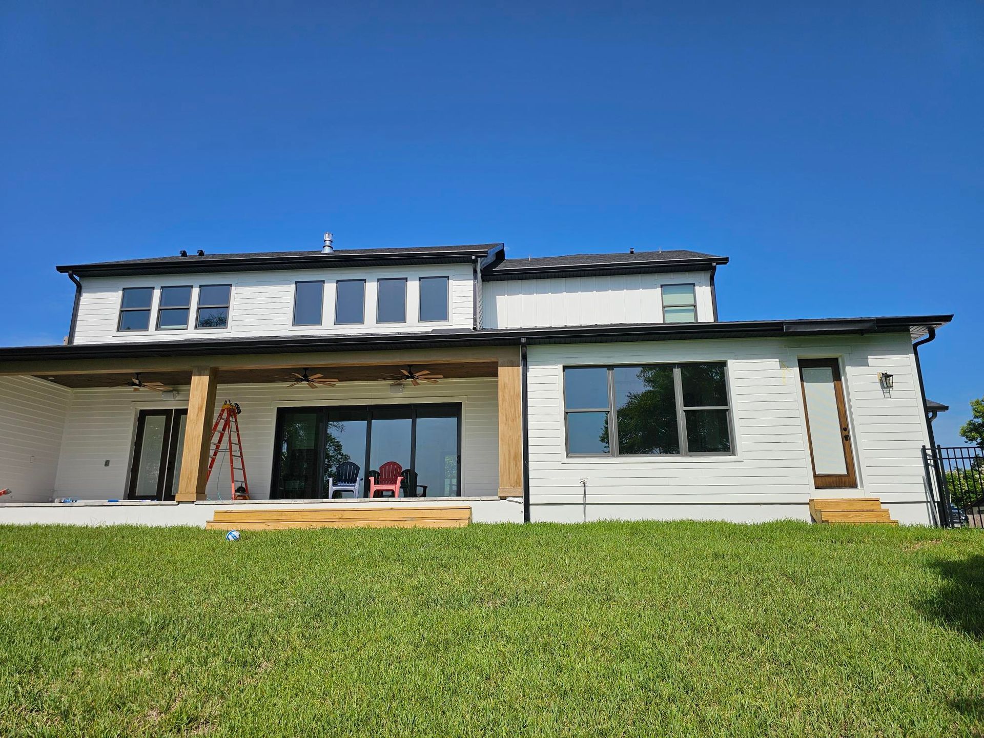 White two-story house with a large front porch and green lawn under a blue sky