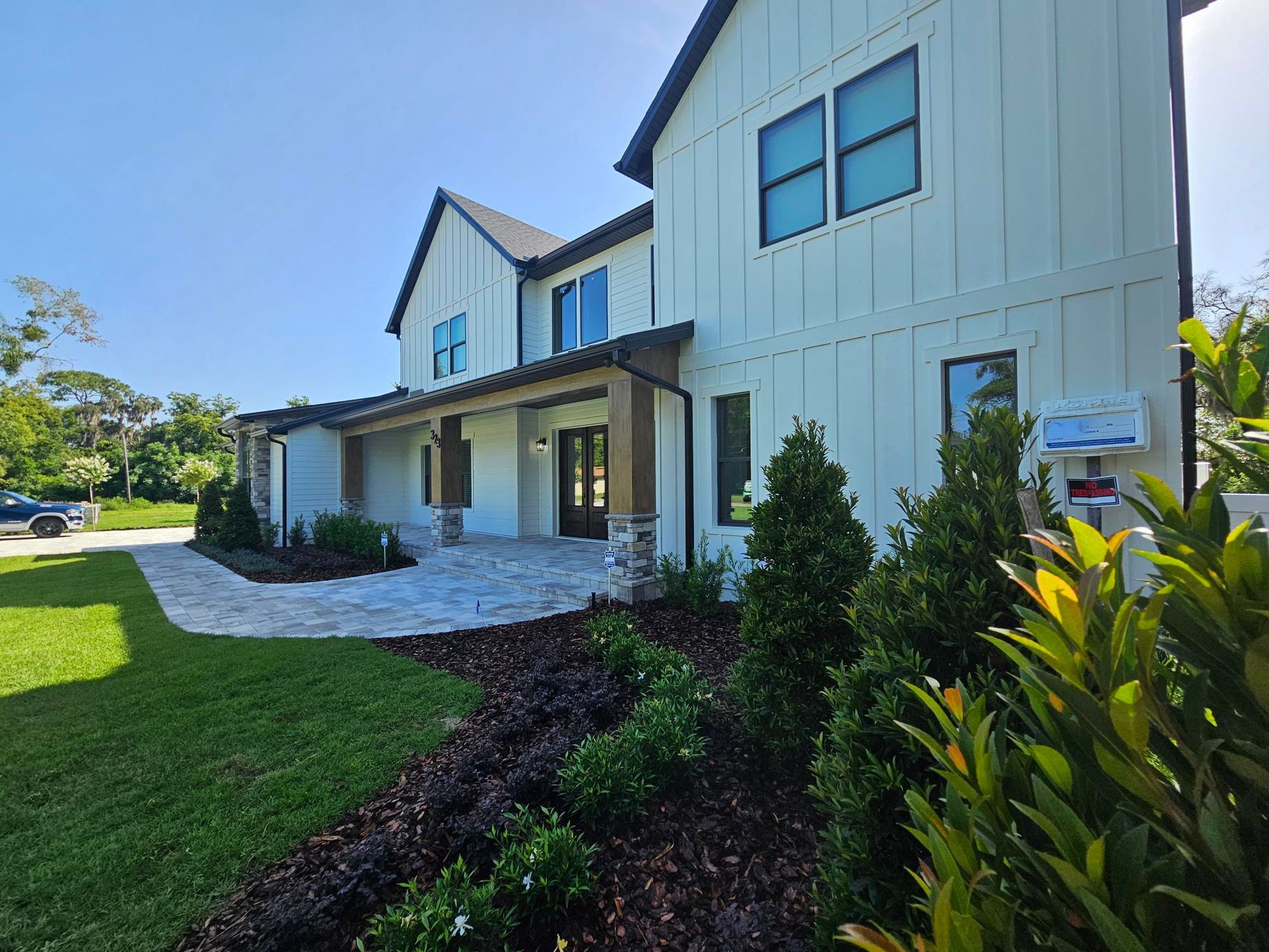Modern two-story white house with a front porch, blue sky, and landscaped lawn.