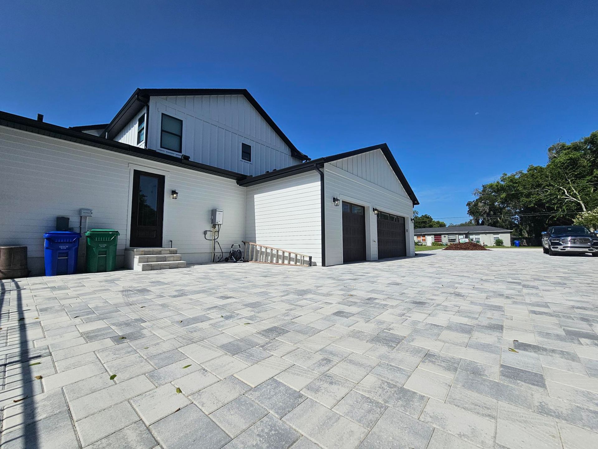 White industrial building with garage doors and a large paved driveway under a blue sky